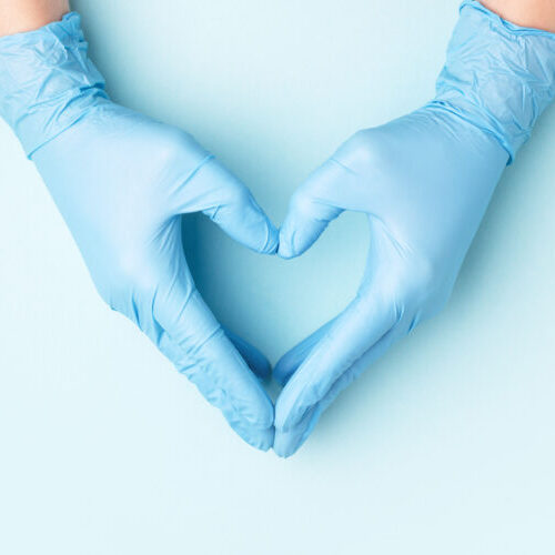 Doctor's hands in medical gloves in shape of heart on blue background. Banner for website with copy space.